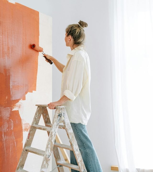 A Woman on a Ladder Painting a Wall